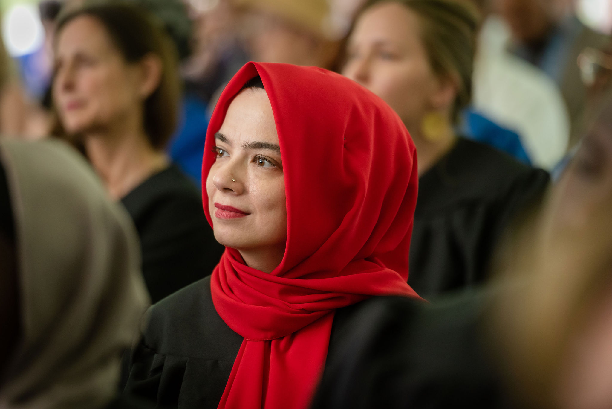 A graduate wearing a red hijab listening