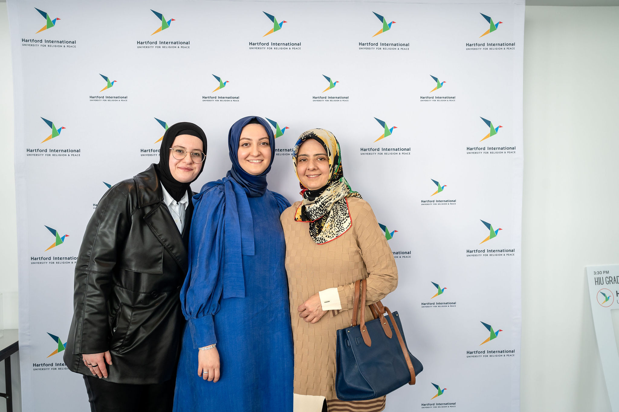 3 women in hijab in front of HIU banner