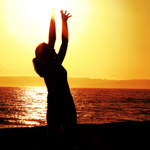 Silhouette of woman reaching toward sun